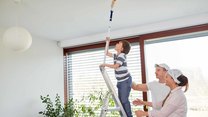 young boy on ladder (parents behind him), painting ceiling