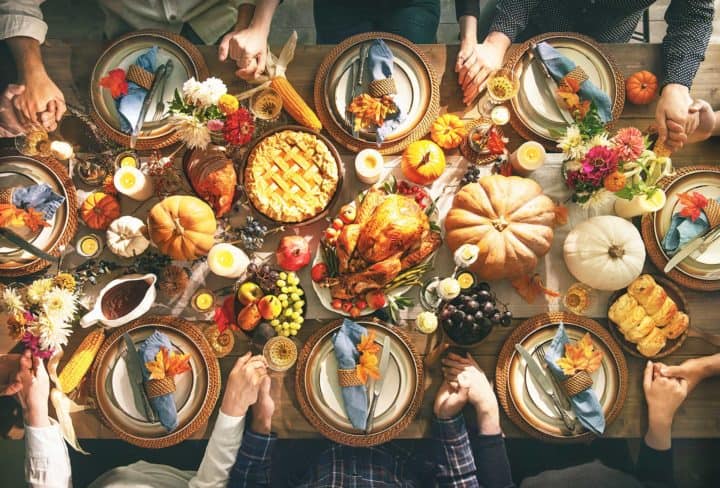 Thanksgiving table laden with food & surrounded by people holding hands